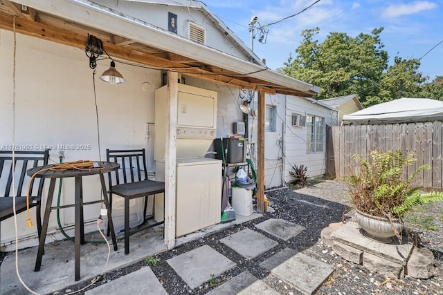 view of exterior entry with a patio area, fence, and stacked washer and dryer