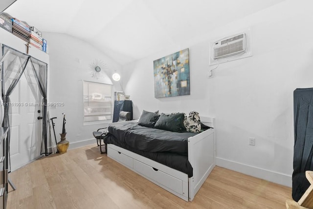 bedroom with a wall unit AC, baseboards, light wood-style floors, and vaulted ceiling