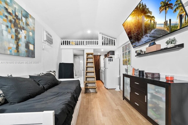 bedroom with a wall unit AC, light wood-style floors, freestanding refrigerator, and high vaulted ceiling