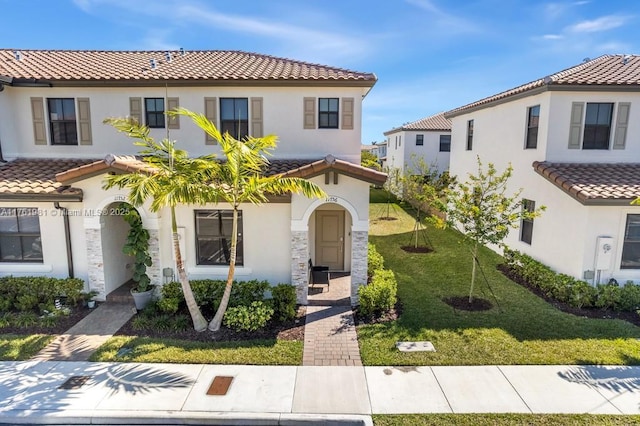 mediterranean / spanish home featuring a front lawn, a tile roof, and stucco siding