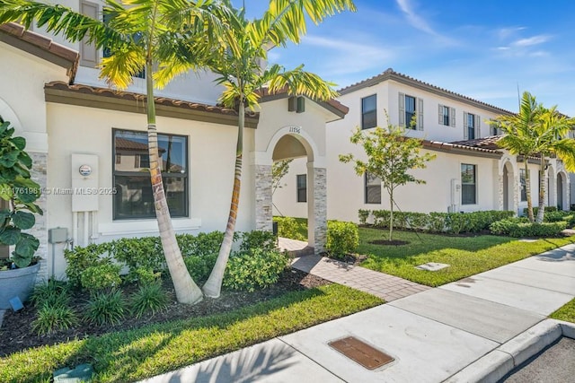 view of front facade with a front yard, a tile roof, and stucco siding