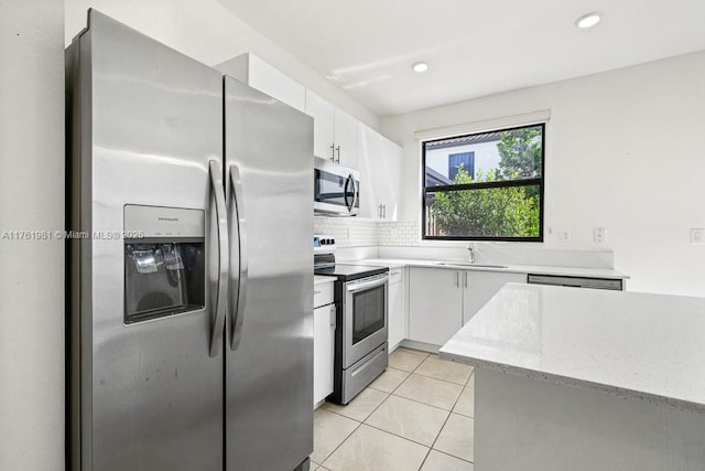 kitchen with a sink, backsplash, stainless steel appliances, white cabinets, and light tile patterned floors