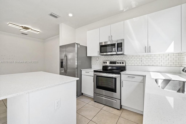 kitchen with a sink, light stone counters, tasteful backsplash, appliances with stainless steel finishes, and white cabinets