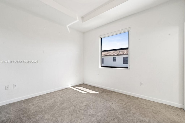 carpeted spare room with a tray ceiling and baseboards