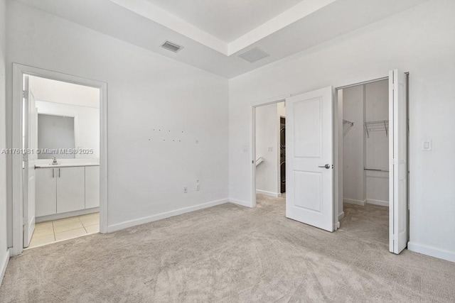 unfurnished bedroom featuring visible vents, a tray ceiling, a spacious closet, light carpet, and connected bathroom