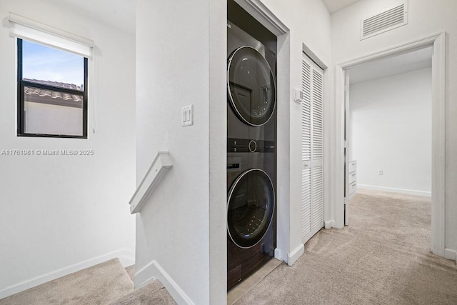 laundry area with visible vents, baseboards, light colored carpet, laundry area, and stacked washer / drying machine