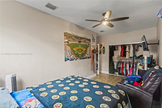 bedroom with a textured ceiling, wood finished floors, a closet, ceiling fan, and visible vents