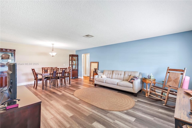 living area featuring visible vents, a textured ceiling, light wood-type flooring, and baseboards