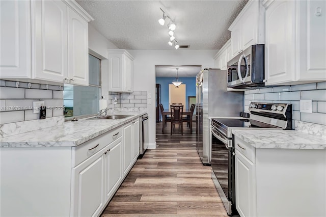 kitchen featuring a sink, stainless steel appliances, white cabinets, a textured ceiling, and light wood-type flooring