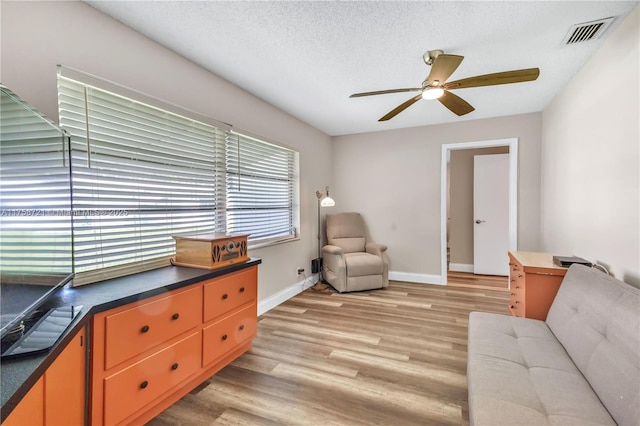 sitting room featuring visible vents, light wood-style flooring, a textured ceiling, and a ceiling fan