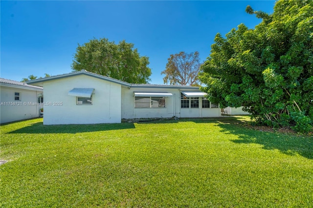 rear view of house featuring a lawn and stucco siding