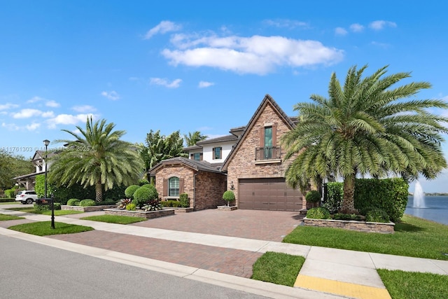 view of front of house with decorative driveway, stone siding, a garage, and a water view