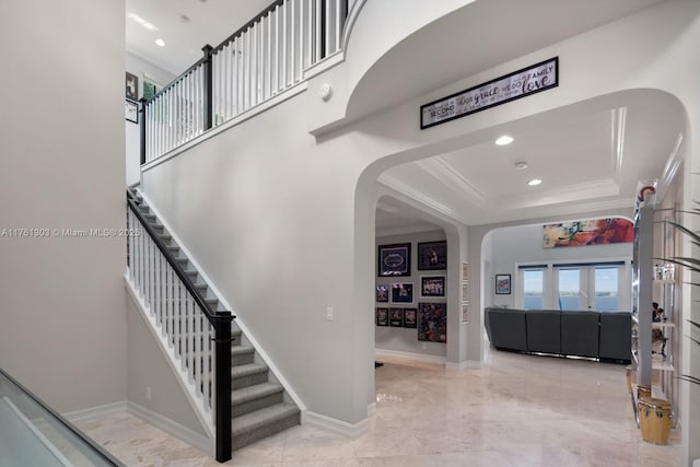 foyer with baseboards, recessed lighting, arched walkways, ornamental molding, and a raised ceiling