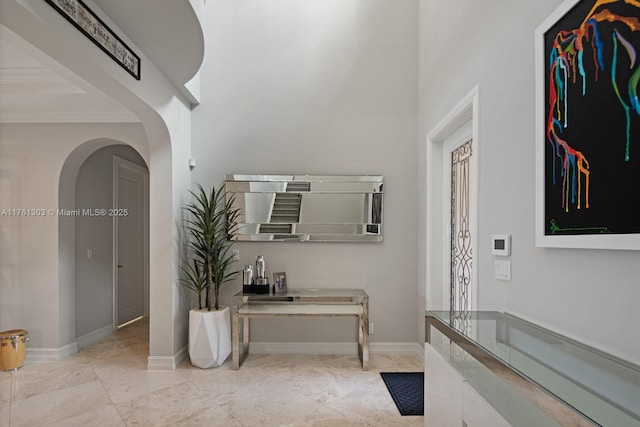 hall with arched walkways, crown molding, a high ceiling, and baseboards