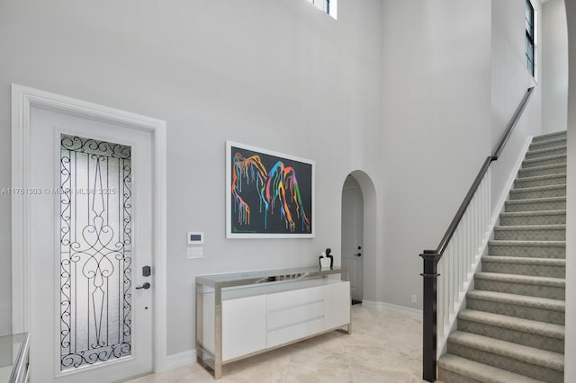 entryway with stairs, a high ceiling, baseboards, and arched walkways