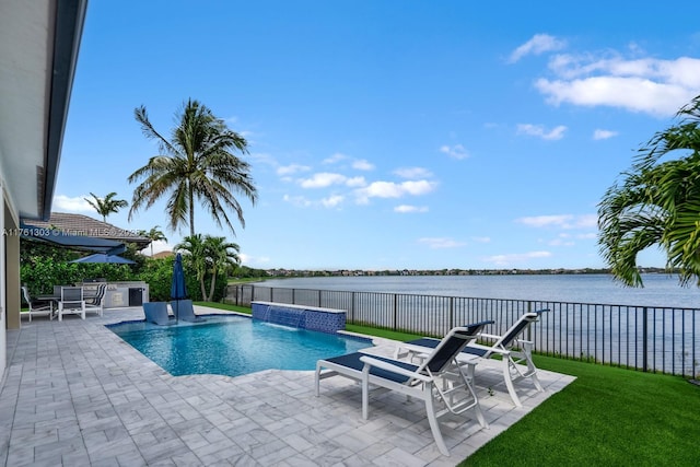 view of swimming pool with a patio area, an outdoor kitchen, a fenced backyard, and a water view