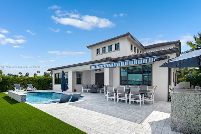 back of house featuring outdoor dining space, a patio, a fenced in pool, exterior kitchen, and stucco siding