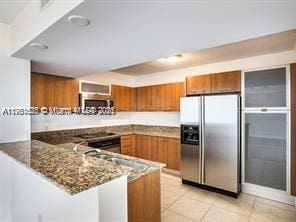 kitchen featuring a peninsula, light tile patterned flooring, stone countertops, stainless steel appliances, and brown cabinets