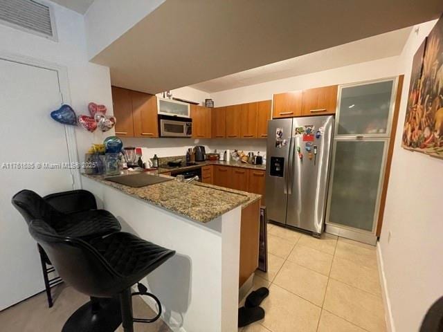 kitchen featuring visible vents, light tile patterned floors, brown cabinets, appliances with stainless steel finishes, and a peninsula