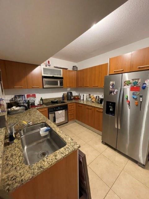 kitchen with brown cabinets, a sink, stainless steel appliances, stone counters, and light tile patterned floors