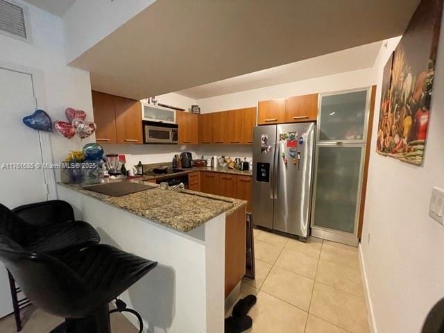 kitchen with visible vents, brown cabinets, appliances with stainless steel finishes, a peninsula, and light tile patterned flooring