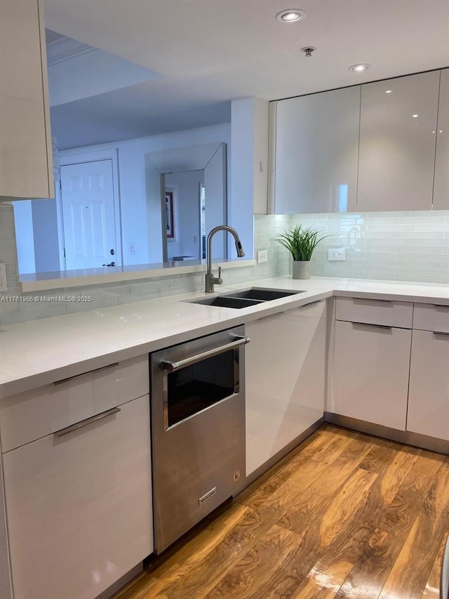 kitchen featuring modern cabinets, a sink, wood finished floors, white cabinets, and light countertops