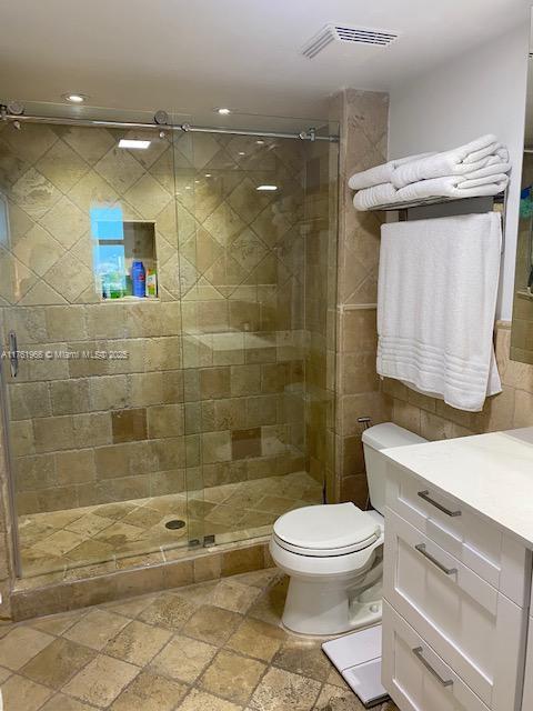 full bath with vanity, visible vents, stone tile flooring, a shower stall, and toilet