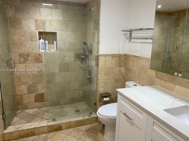 bathroom with vanity, a wainscoted wall, a stall shower, tile walls, and toilet