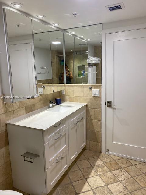 bathroom featuring vanity, visible vents, recessed lighting, tile walls, and backsplash