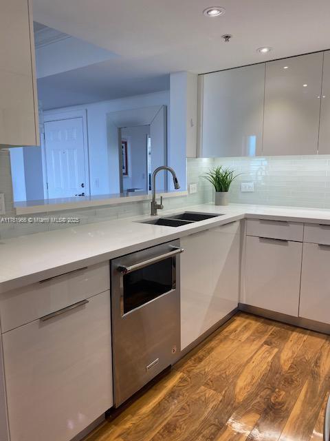 kitchen with a sink, light countertops, dishwasher, light wood-style floors, and white cabinetry