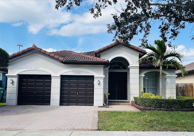 mediterranean / spanish house featuring fence, a tiled roof, stucco siding, decorative driveway, and a garage