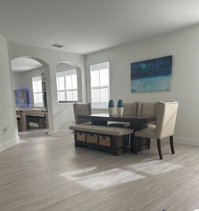 dining space with wood finished floors, visible vents, baseboards, arched walkways, and a textured ceiling