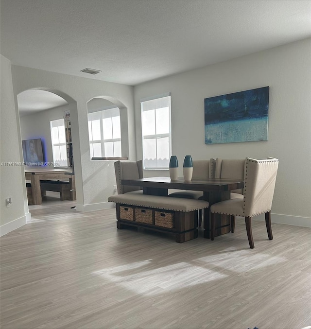 dining room with visible vents, baseboards, wood finished floors, arched walkways, and a textured ceiling