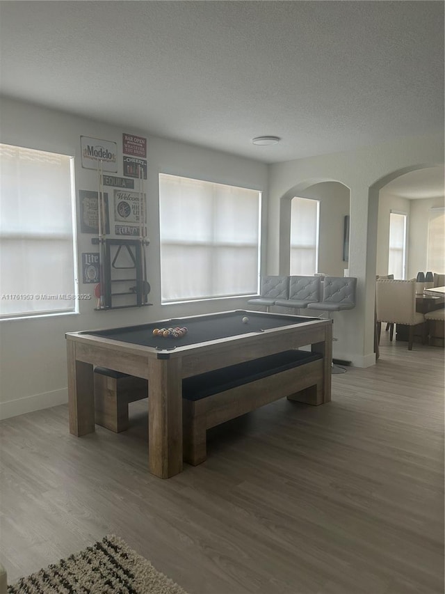 game room with baseboards, a textured ceiling, wood finished floors, and arched walkways