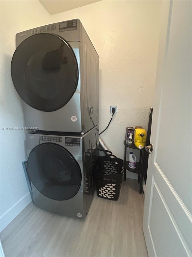 laundry room featuring laundry area, stacked washing maching and dryer, baseboards, and wood finished floors