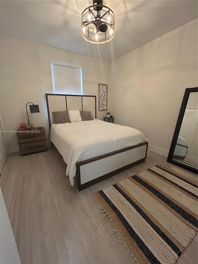 bedroom with a notable chandelier, baseboards, a textured ceiling, and wood finished floors