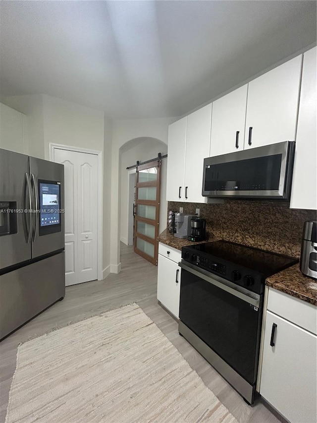 kitchen with tasteful backsplash, stainless steel appliances, a barn door, arched walkways, and white cabinets