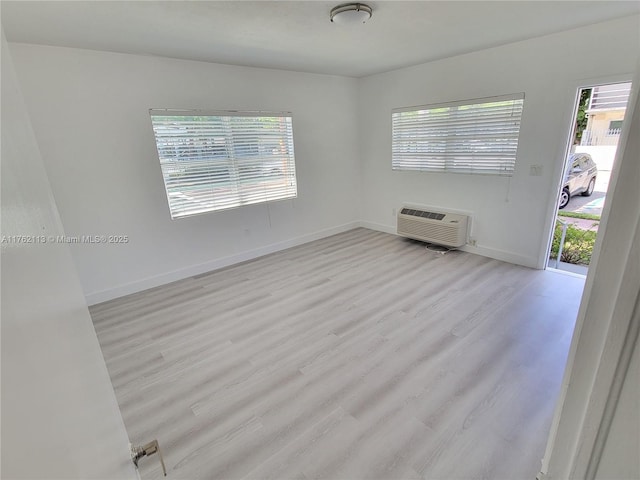 empty room featuring a wall unit AC, baseboards, and wood finished floors