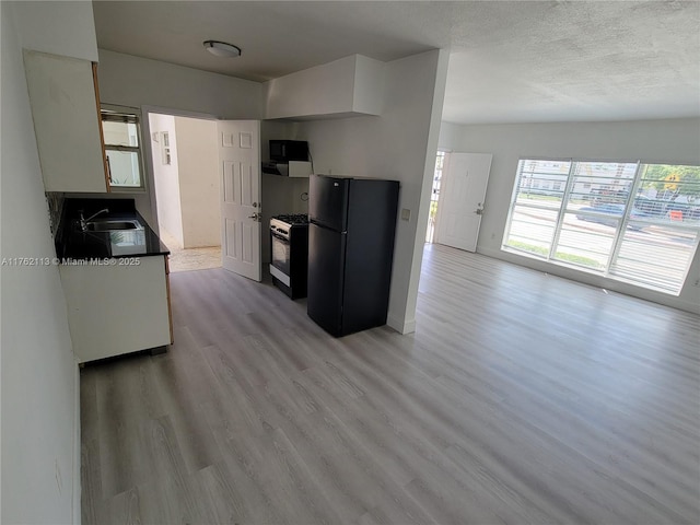 kitchen featuring light wood-style flooring, freestanding refrigerator, a sink, gas range oven, and a textured ceiling