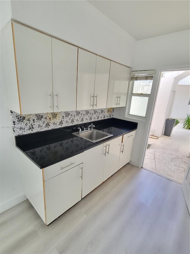 kitchen with dark countertops, white cabinets, light wood-style floors, and a sink