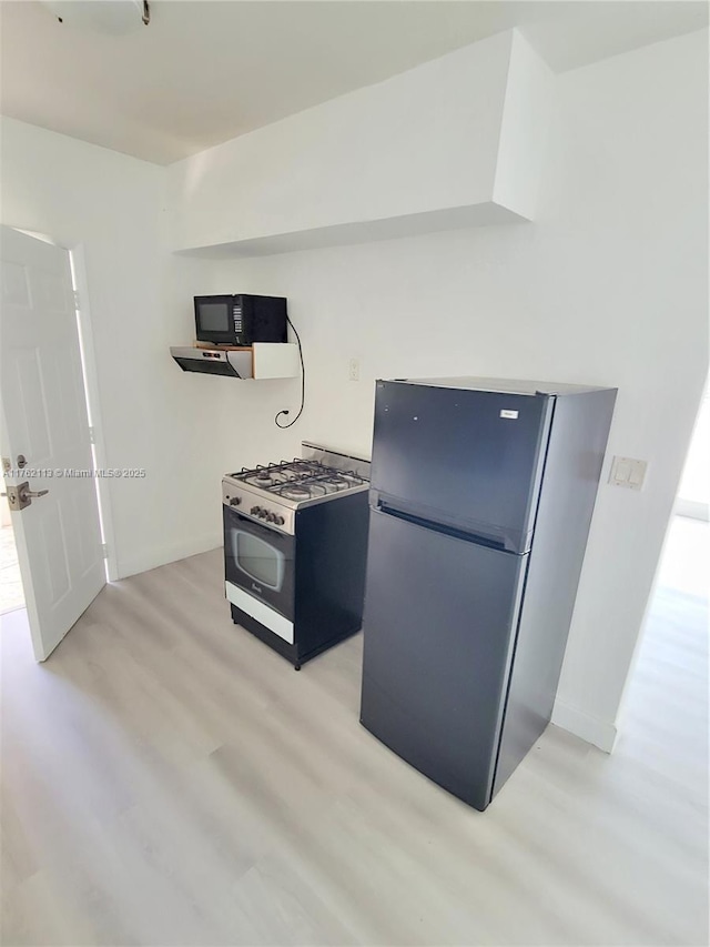 kitchen with light wood-type flooring, freestanding refrigerator, baseboards, black microwave, and gas range