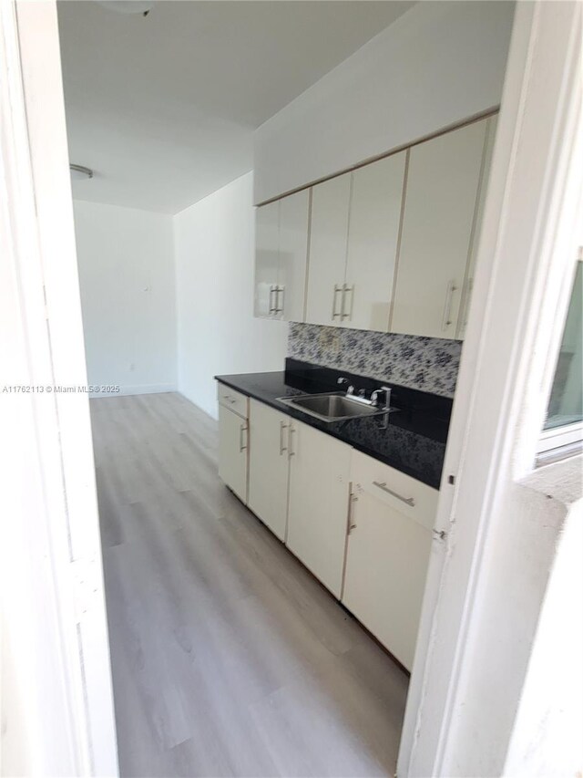 kitchen with a sink, light wood-type flooring, dark countertops, and backsplash