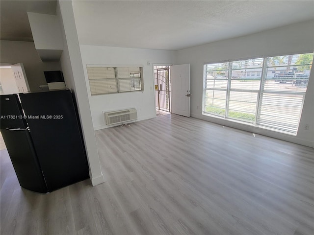 unfurnished living room with baseboards, wood finished floors, and a wall mounted AC