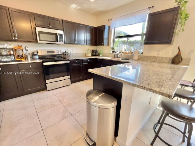 kitchen featuring light stone countertops, a breakfast bar, a peninsula, light tile patterned flooring, and stainless steel appliances