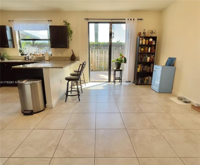 kitchen with dark brown cabinets, baseboards, a breakfast bar area, light tile patterned floors, and a peninsula