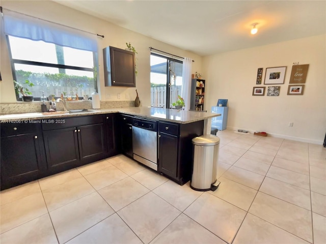 kitchen featuring a sink, a peninsula, light tile patterned floors, light stone countertops, and dishwasher