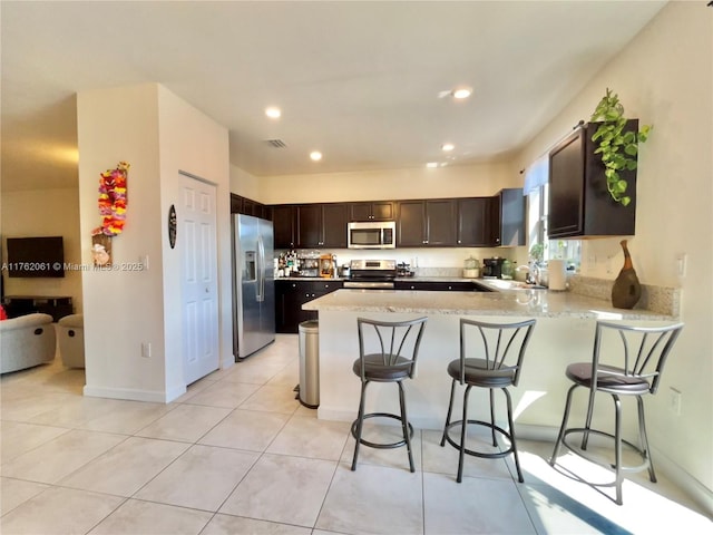 kitchen featuring a sink, appliances with stainless steel finishes, a peninsula, light tile patterned floors, and dark brown cabinets