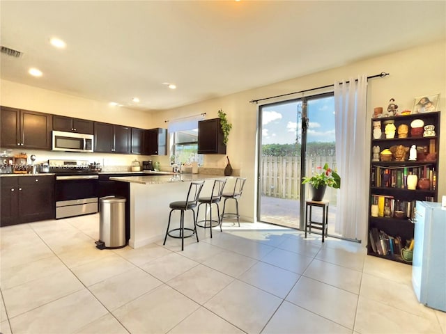 kitchen with visible vents, dark brown cabinets, a breakfast bar area, light countertops, and appliances with stainless steel finishes