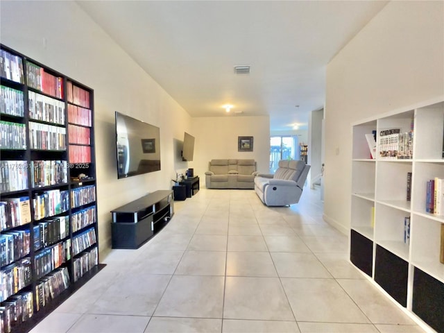 living area featuring tile patterned flooring, wall of books, and visible vents