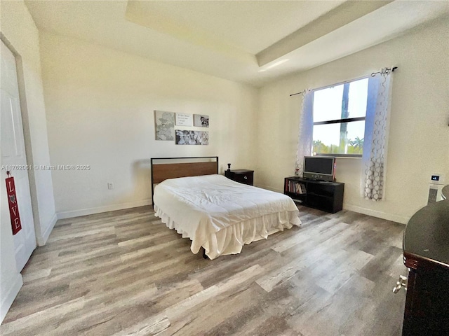 bedroom with a tray ceiling, wood finished floors, and baseboards